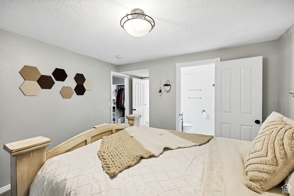 Bedroom featuring ensuite bathroom, a spacious closet, a textured ceiling, baseboards, and a closet
