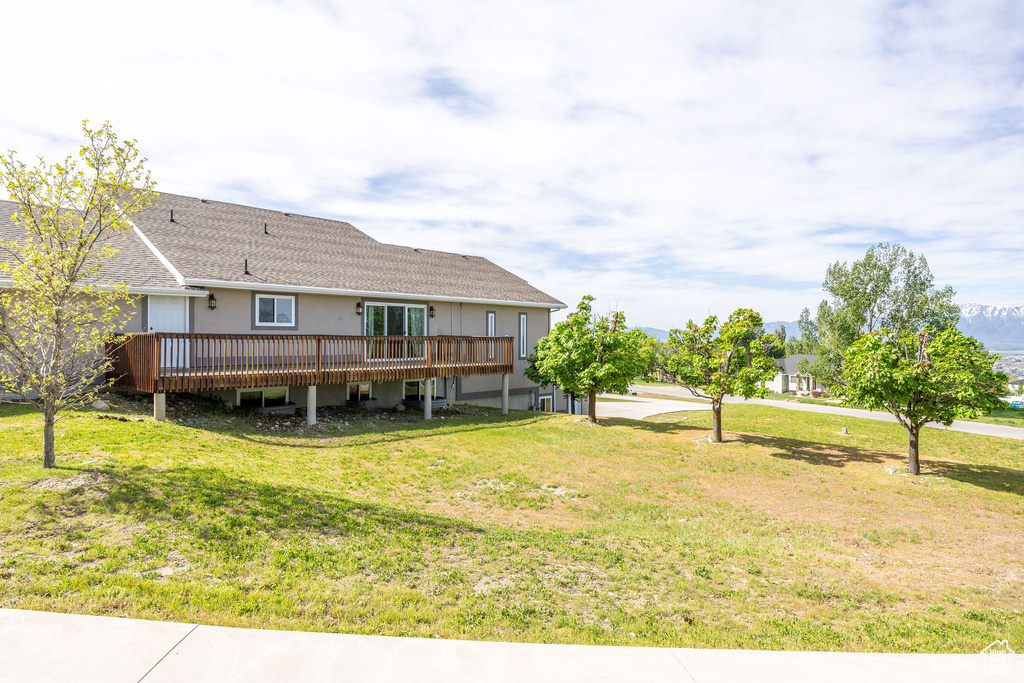 Back of property with a wooden deck, a lawn, and roof with shingles