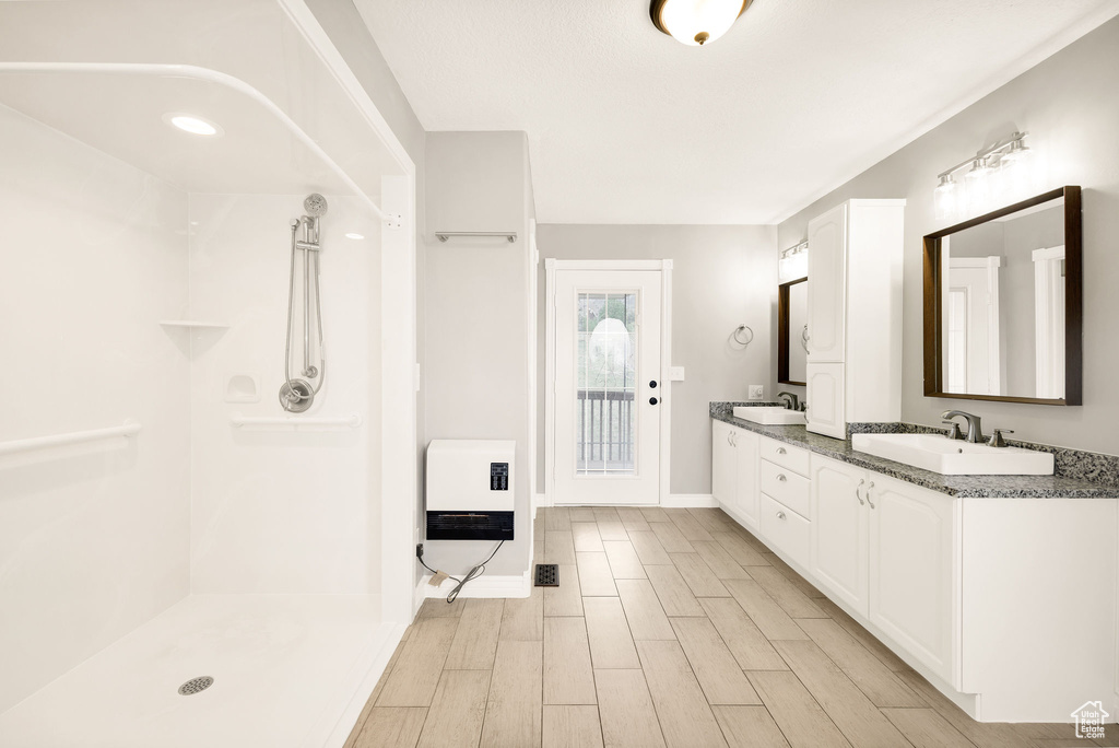 Full bathroom featuring heating unit, double vanity, wood finished floors, a shower, and baseboards