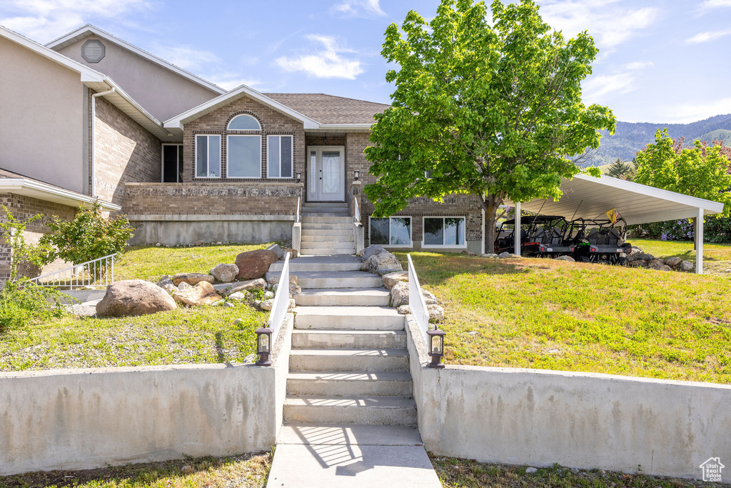 View of front of home with a front yard, brick siding, a carport, and a mountain view