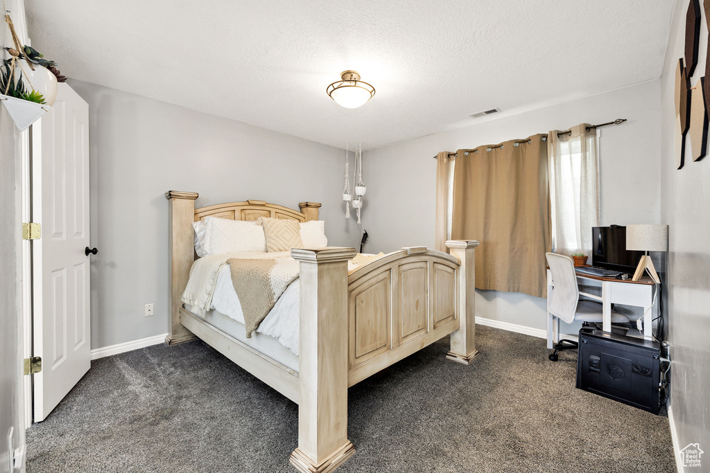 Bedroom featuring dark carpet, baseboards, a textured ceiling, and a desk