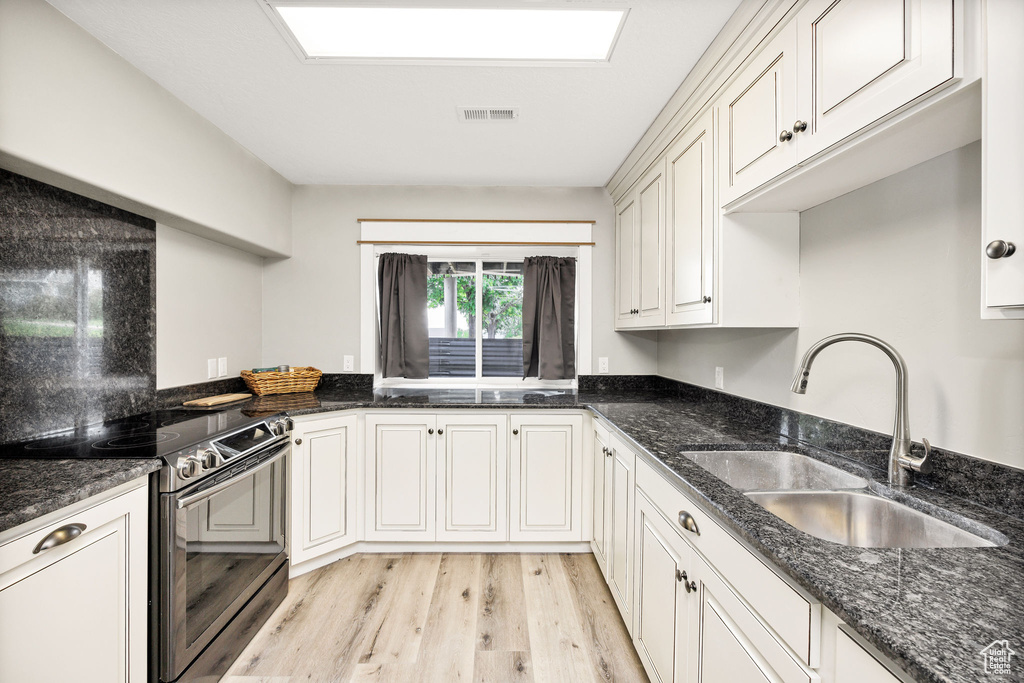 Kitchen featuring electric stove, a sink, light wood-type flooring, dark stone countertops, and white cabinets