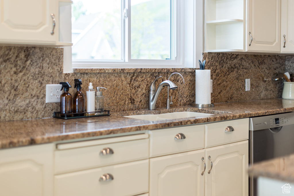 Kitchen with stainless steel dishwasher, a sink, open shelves, white cabinetry, and backsplash