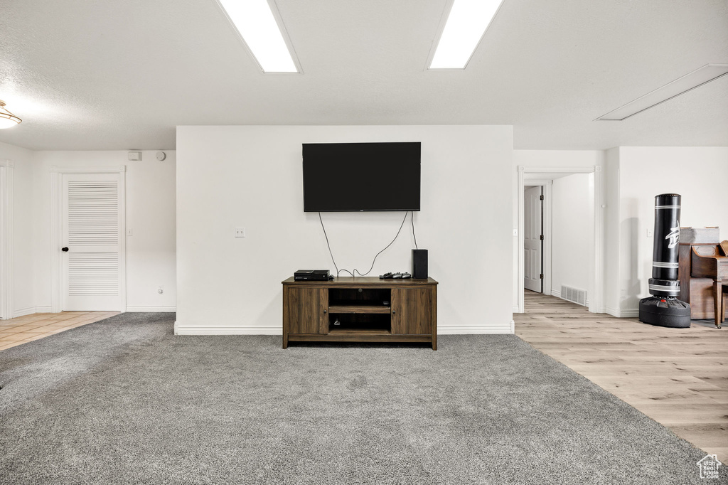 Unfurnished living room featuring attic access, baseboards, carpet flooring, and wood finished floors