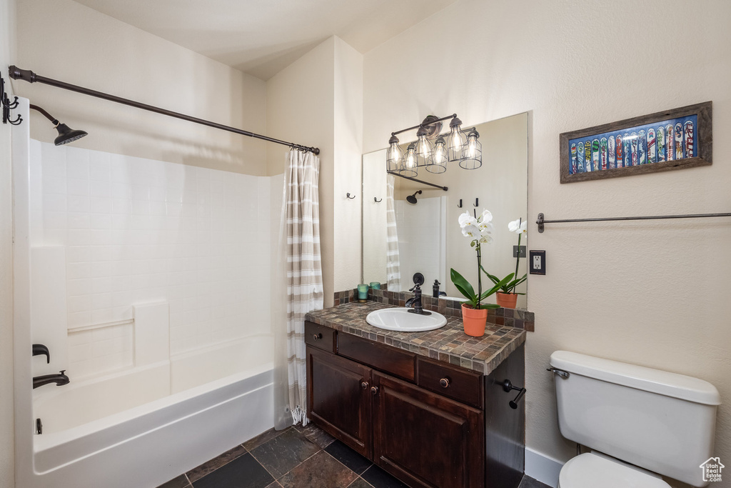 Bathroom featuring toilet, shower / bathtub combination with curtain, stone finish floors, and vanity