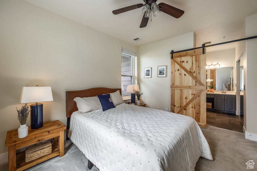 Bedroom featuring a barn door, carpet flooring, ensuite bathroom, and a ceiling fan