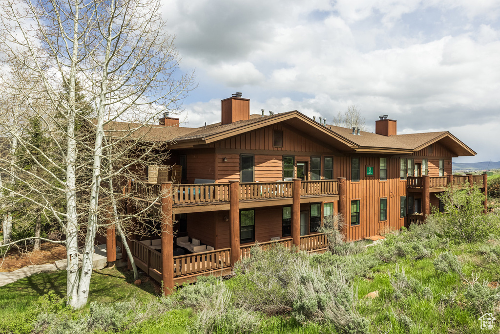 Back of house featuring a chimney, a balcony, a deck, and a shingled roof