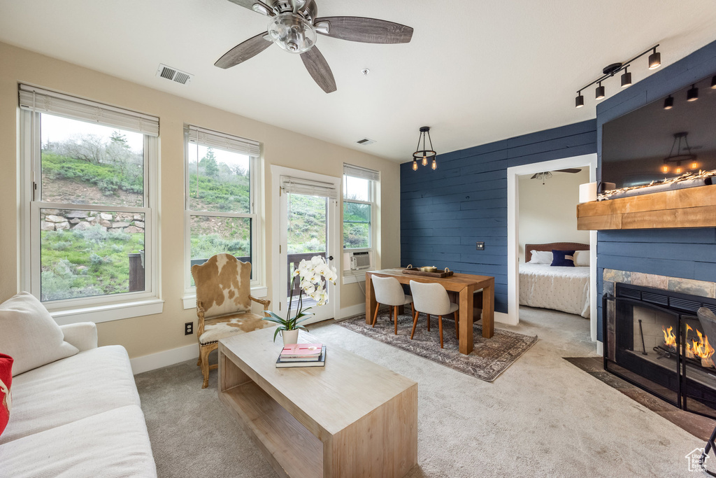 Carpeted living area featuring a fireplace with flush hearth, baseboards, wooden walls, and ceiling fan