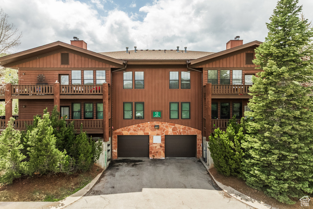 Back of house featuring a chimney, asphalt driveway, an attached garage, and stone siding