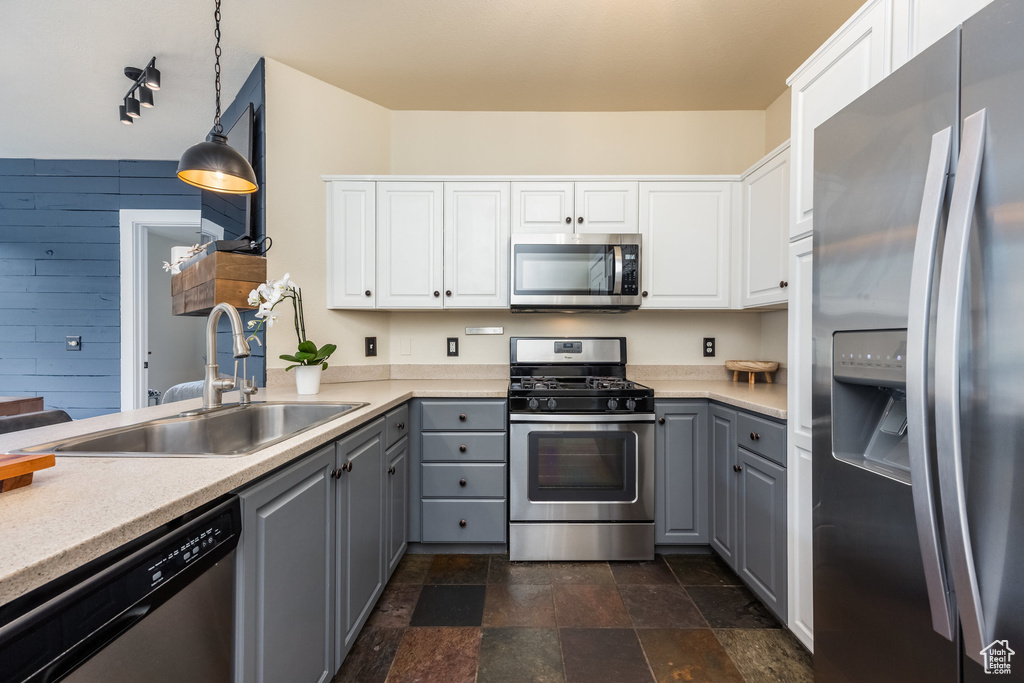 Kitchen with stainless steel appliances, gray cabinetry, a sink, stone finish flooring, and wood walls