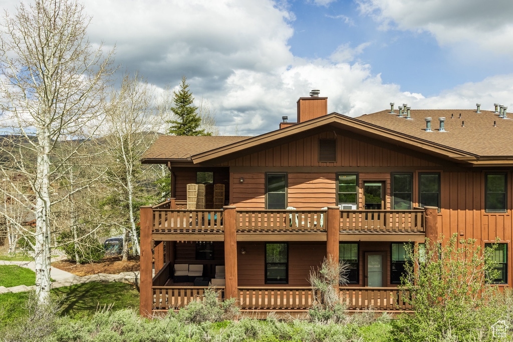 Back of property featuring a chimney, roof with shingles, board and batten siding, and a balcony