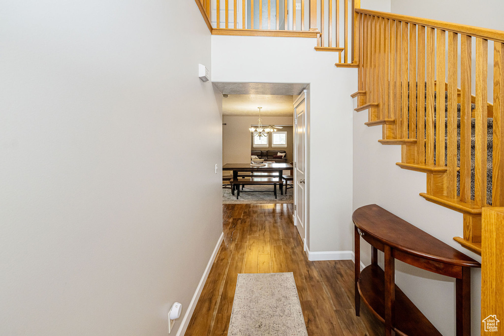 Corridor with baseboards, wood finished floors, stairway, and a chandelier