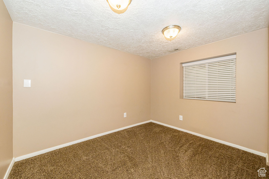 Empty room featuring dark colored carpet, a textured ceiling, and baseboards