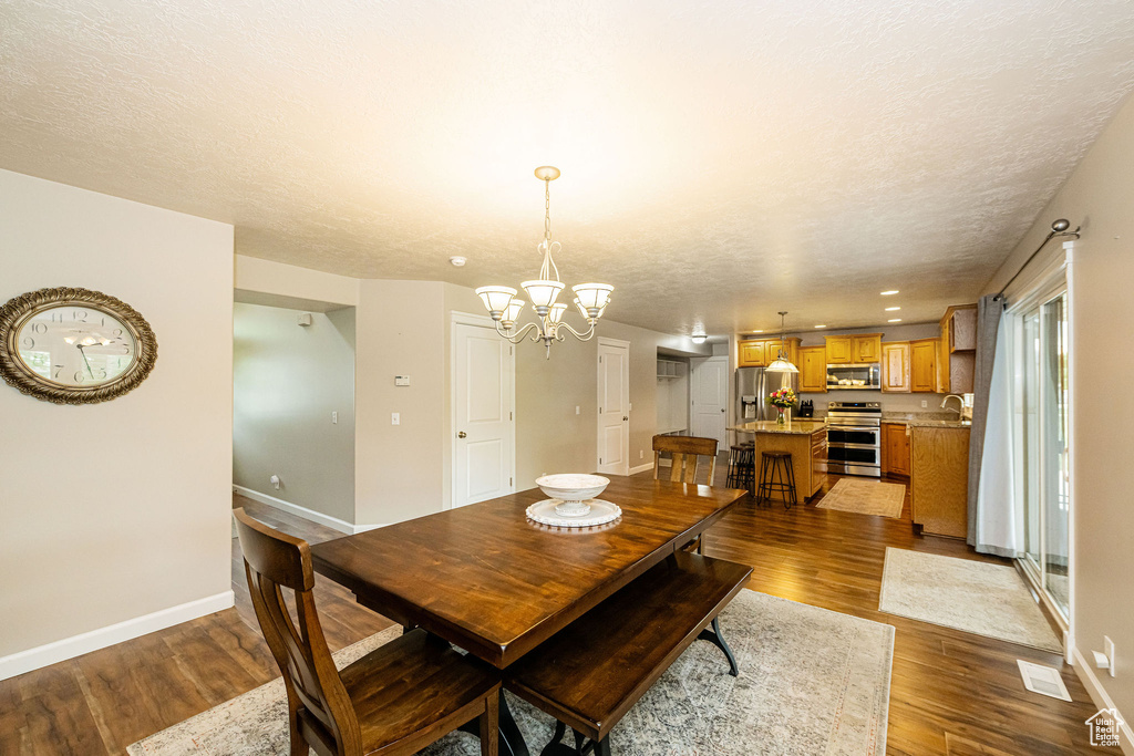 Dining area with a chandelier, dark wood-type flooring, baseboards, and a textured ceiling