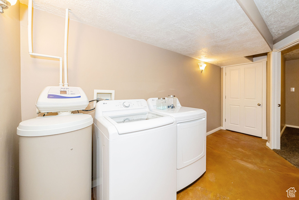 Laundry area featuring a textured ceiling, independent washer and dryer, light colored carpet, and baseboards