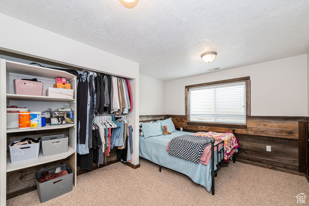 Bedroom featuring light carpet, a textured ceiling, and wainscoting