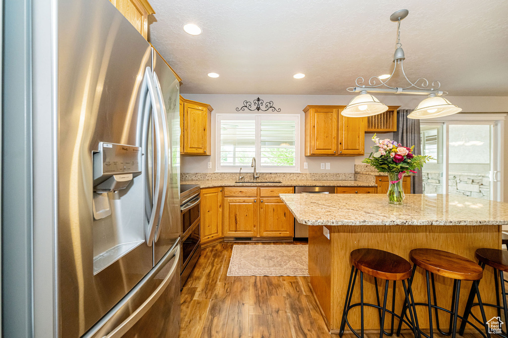 Kitchen featuring appliances with stainless steel finishes, a sink, wood finished floors, a center island, and a breakfast bar