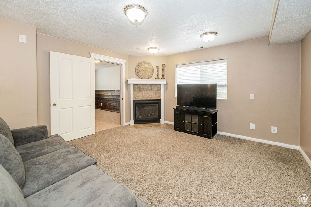 Carpeted living area featuring a tiled fireplace, a textured ceiling, and baseboards