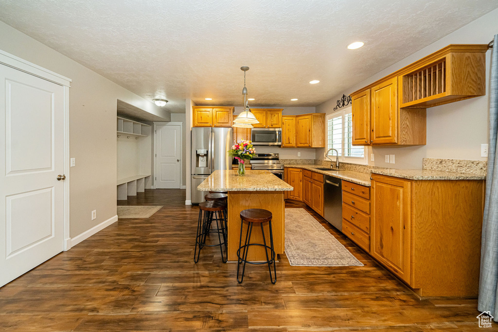 Kitchen featuring stainless steel appliances, a sink, a center island, dark wood-type flooring, and a breakfast bar