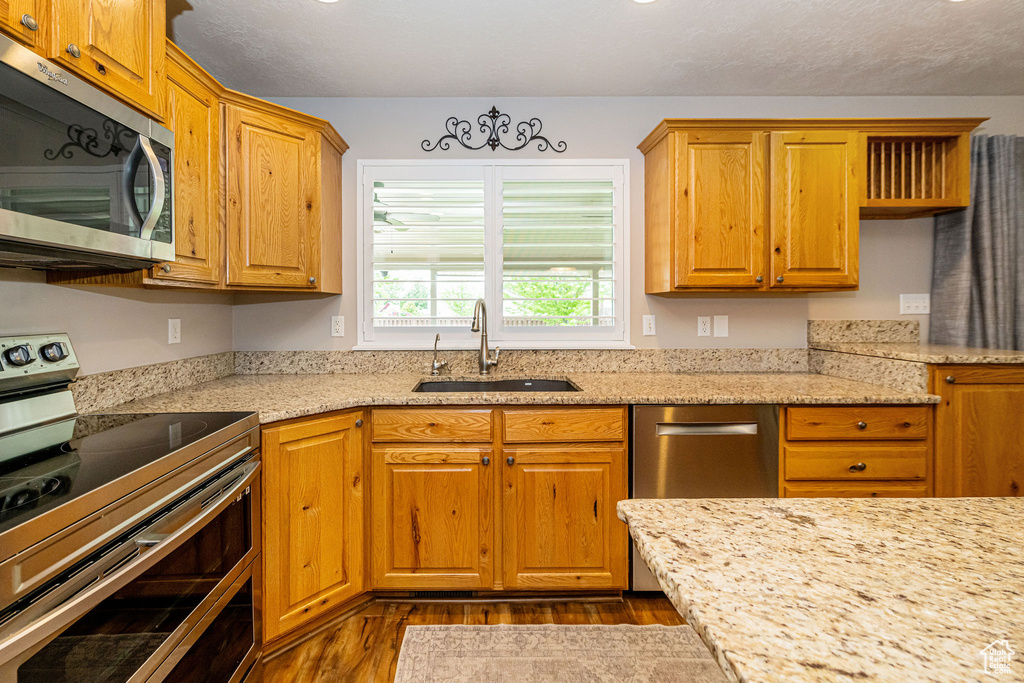 Kitchen featuring stainless steel appliances, a sink, dark wood-type flooring, and light stone counters