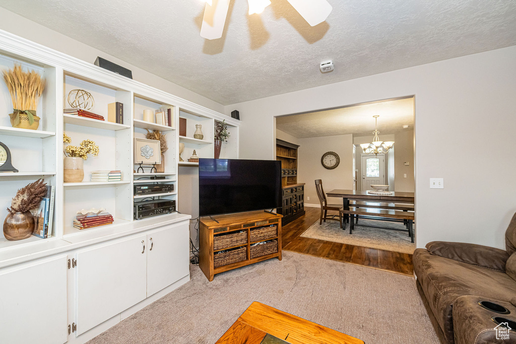 Carpeted living room featuring ceiling fan, a textured ceiling, wood finished floors, and a chandelier