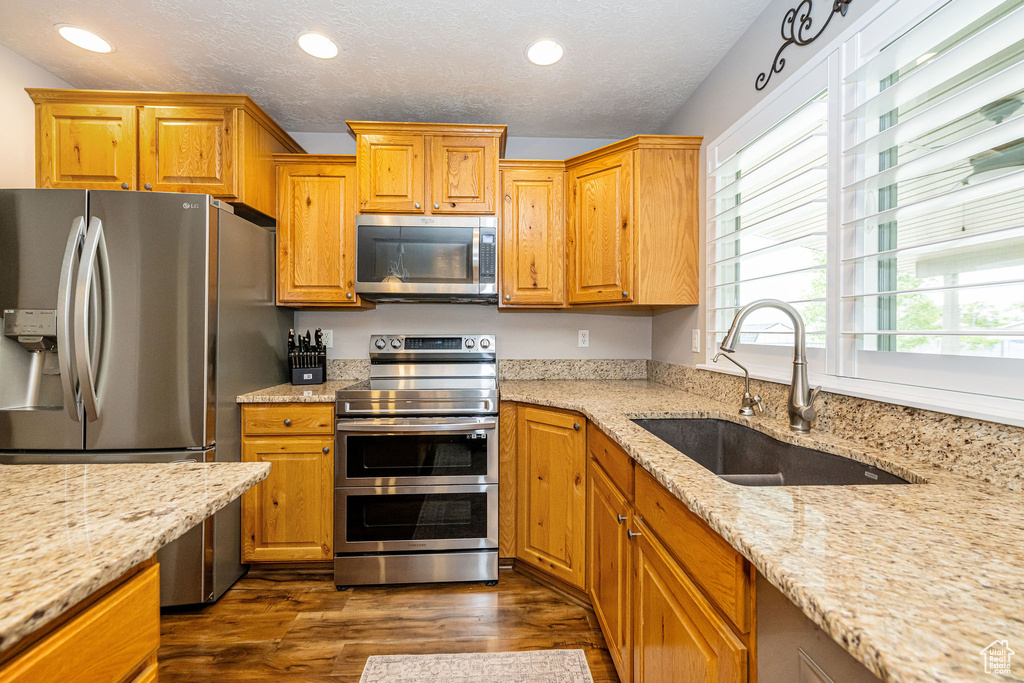Kitchen featuring appliances with stainless steel finishes, a sink, dark wood-style floors, light stone counters, and recessed lighting