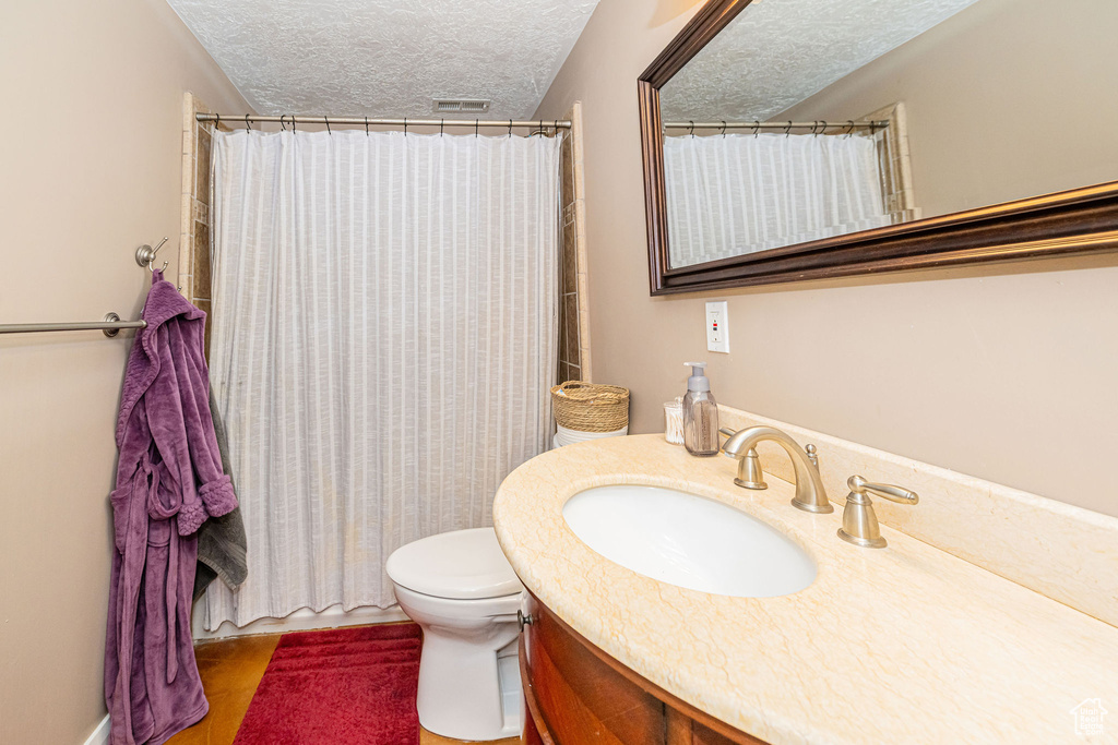 Full bathroom with a textured ceiling, toilet, vanity, a shower with shower curtain, and wood finished floors