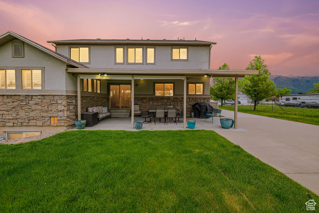 Back of house featuring stone siding, stucco siding, a yard, and a patio