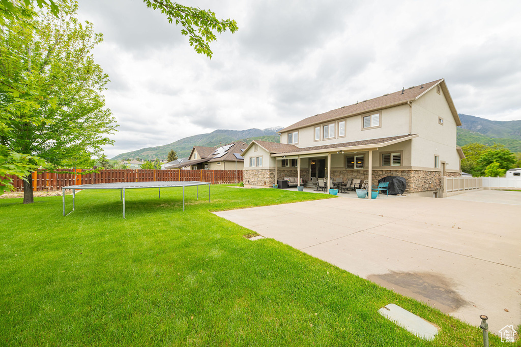 Rear view of house featuring a mountain view, a trampoline, stone siding, and stucco siding