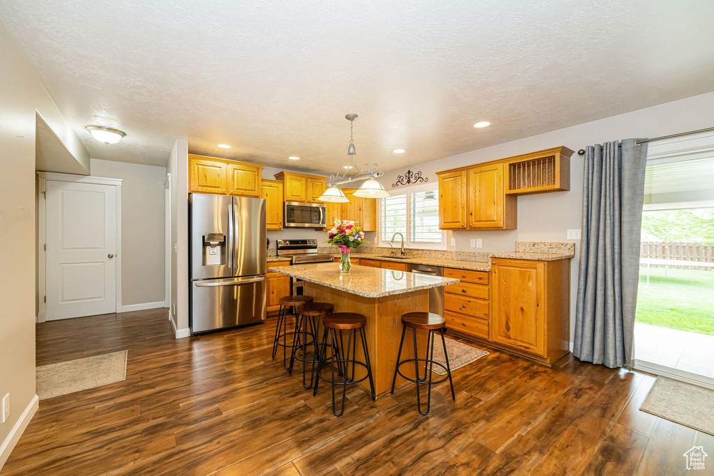 Kitchen featuring appliances with stainless steel finishes, dark wood finished floors, a center island, baseboards, and recessed lighting