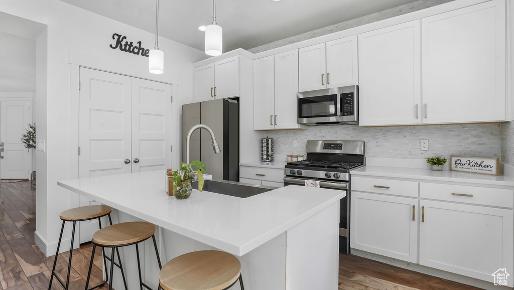 Kitchen with stainless steel appliances, wood finished floors, an island with sink, decorative backsplash, and a kitchen breakfast bar