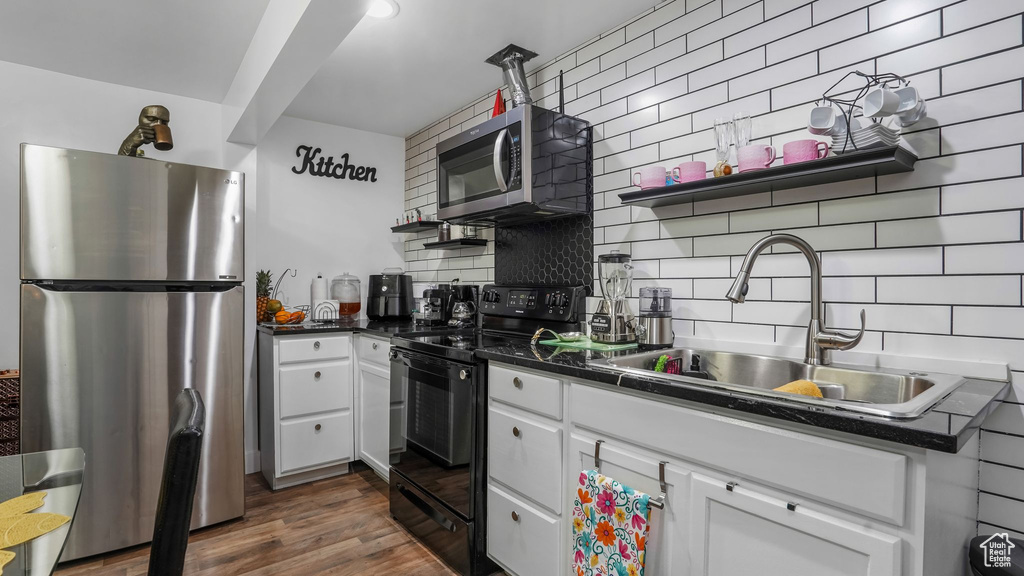 Kitchen featuring stainless steel appliances, a sink, backsplash, and dark countertops