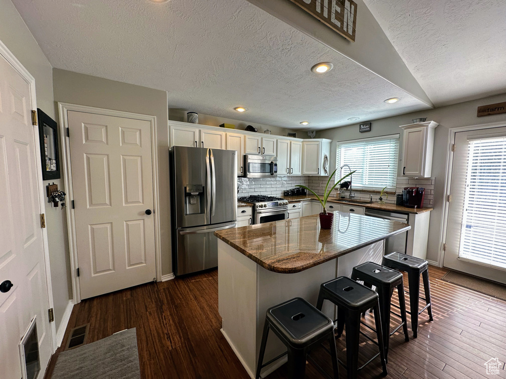 Kitchen with stainless steel appliances, a textured ceiling, a kitchen breakfast bar, white cabinets, and tasteful backsplash