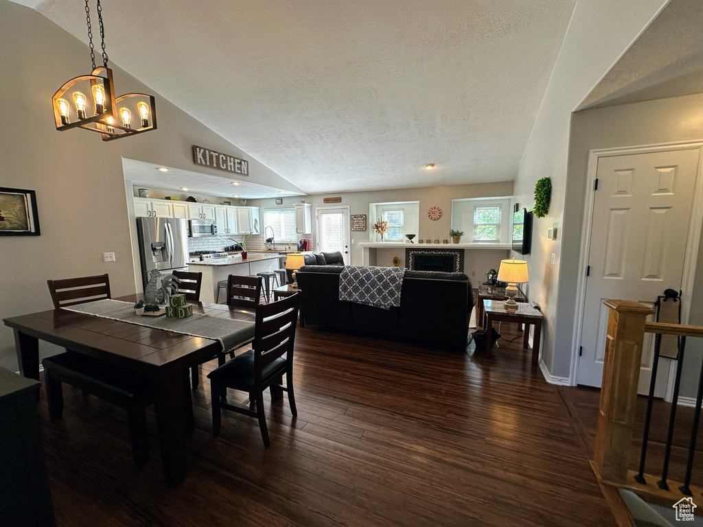 Dining space with dark wood finished floors, a chandelier, lofted ceiling, and a textured ceiling