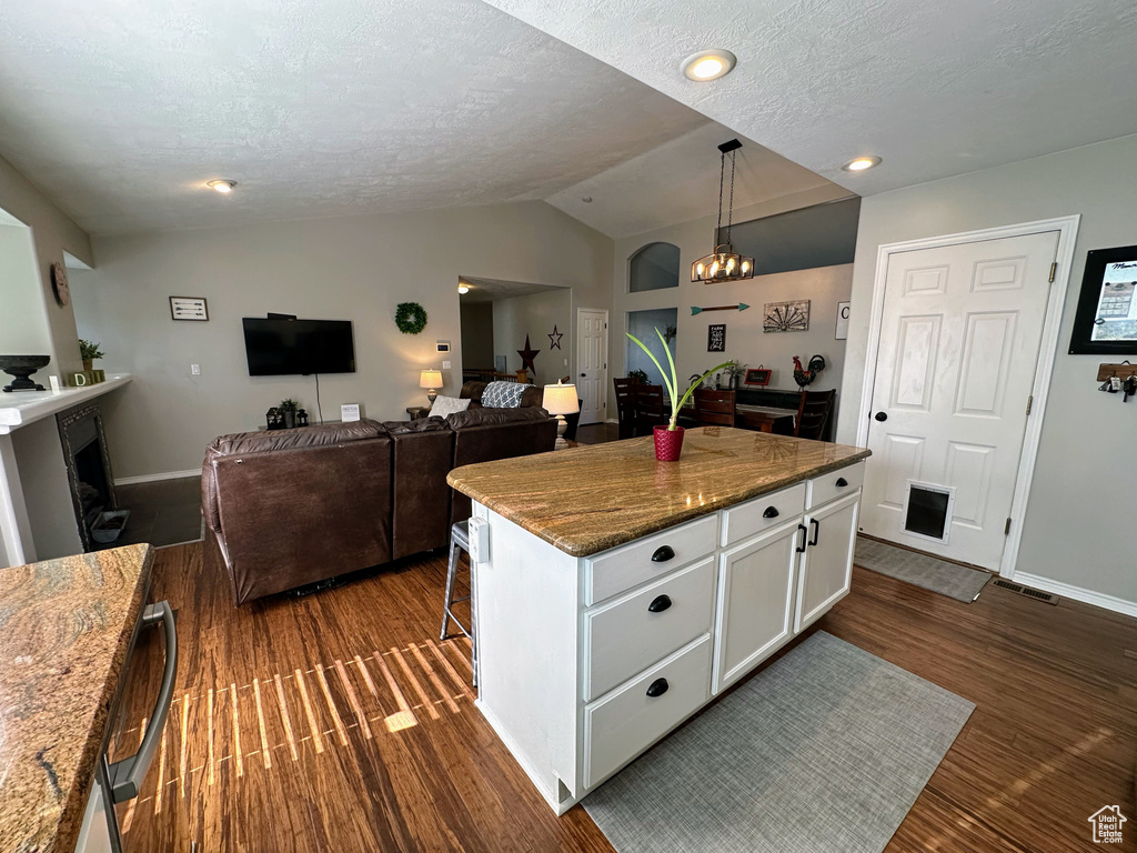 Kitchen featuring lofted ceiling, white cabinets, dark wood-style flooring, a textured ceiling, and a center island