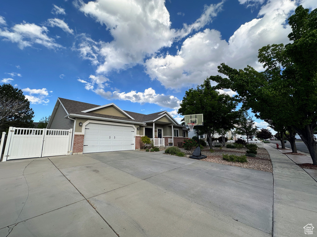 View of front facade featuring brick siding, a garage, concrete driveway, a gate, and covered porch