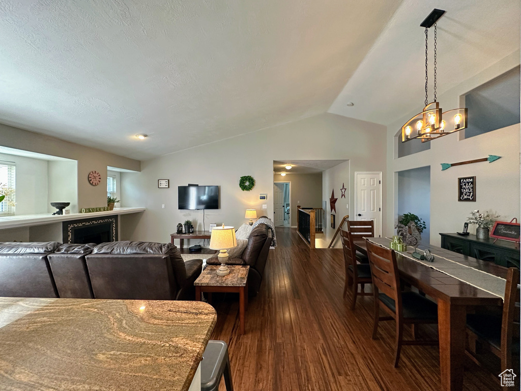 Dining room featuring dark wood-style flooring, a fireplace, vaulted ceiling, and a chandelier