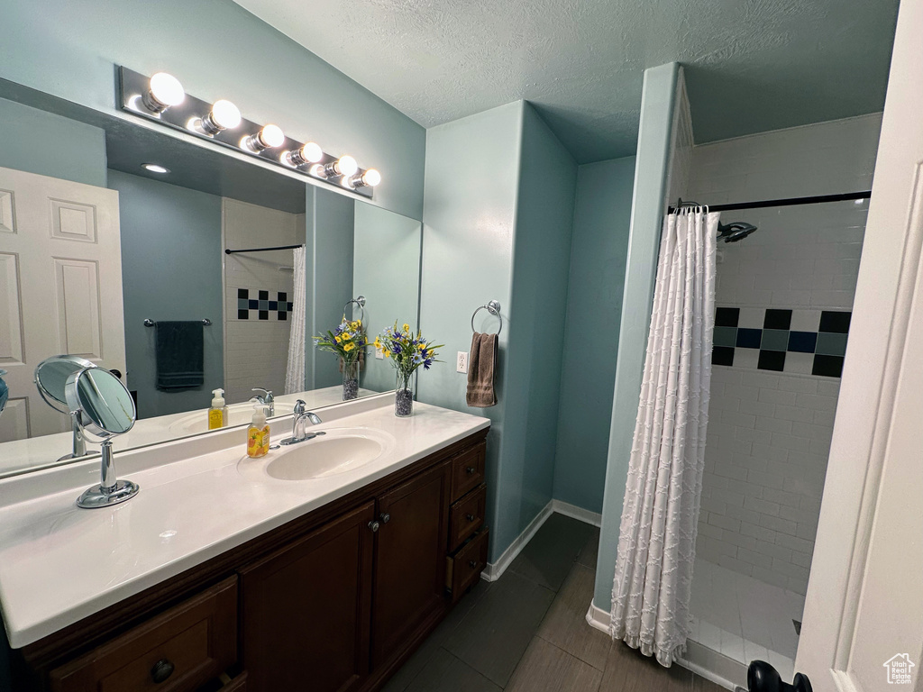 Full bath featuring a tile shower, vanity, a textured ceiling, tile patterned floors, and baseboards