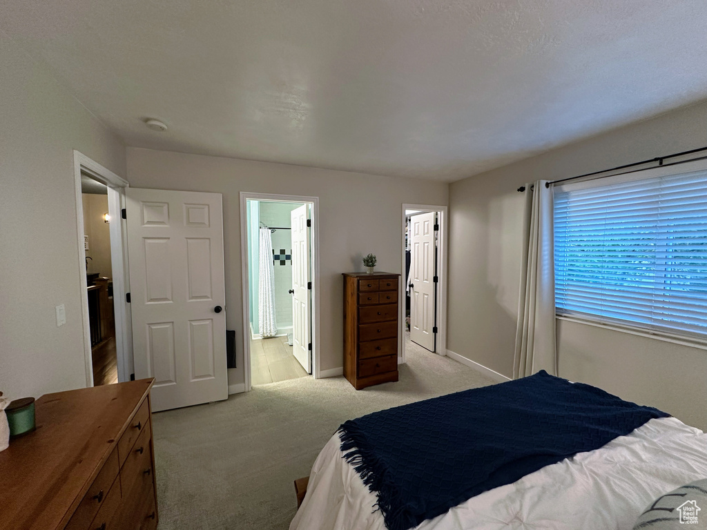 Bedroom with light carpet, ensuite bathroom, baseboards, and a walk in closet