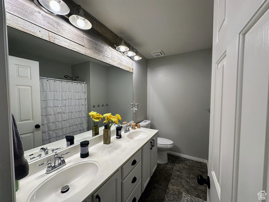 Bathroom featuring toilet, baseboards, double vanity, stone finish floors, and a shower with shower curtain