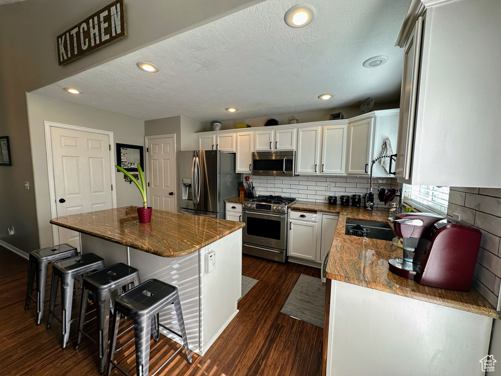 Kitchen featuring appliances with stainless steel finishes, dark wood finished floors, a breakfast bar area, tasteful backsplash, and a textured ceiling