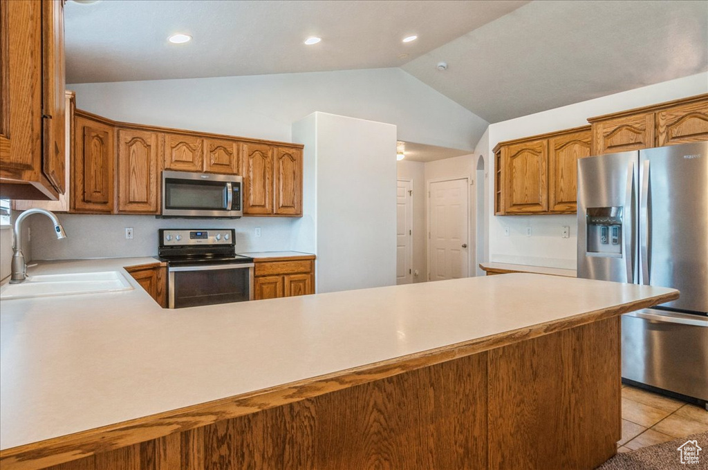 Kitchen with appliances with stainless steel finishes, a sink, vaulted ceiling, light countertops, and brown cabinetry