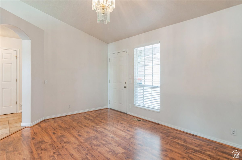 Empty room with arched walkways, wood finished floors, baseboards, and a chandelier
