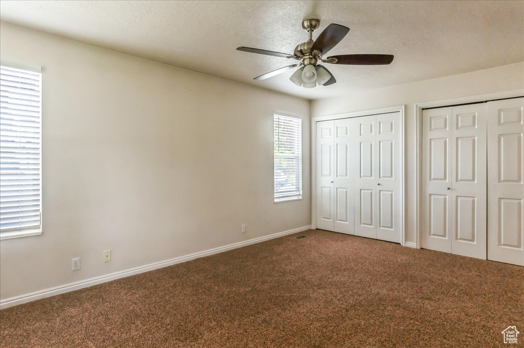 Unfurnished bedroom featuring carpet floors, two closets, baseboards, a textured ceiling, and a ceiling fan