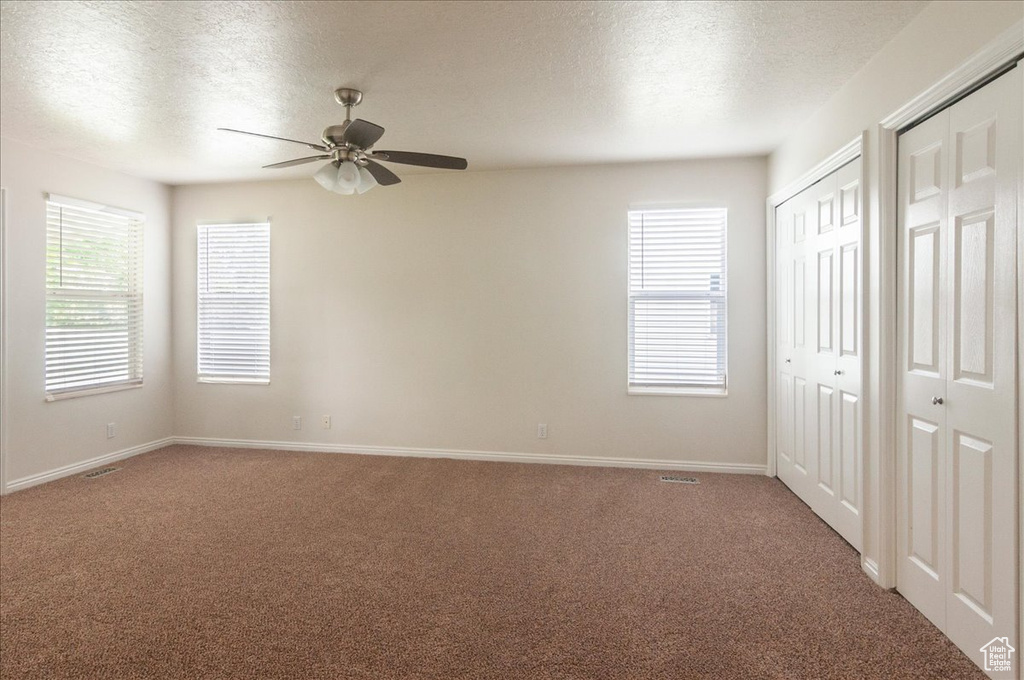 Unfurnished bedroom featuring multiple closets, light colored carpet, a textured ceiling, and baseboards