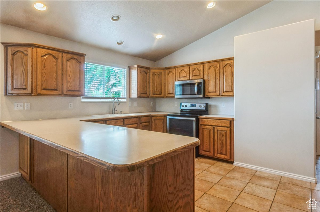 Kitchen with stainless steel appliances, a sink, brown cabinetry, a peninsula, and light countertops