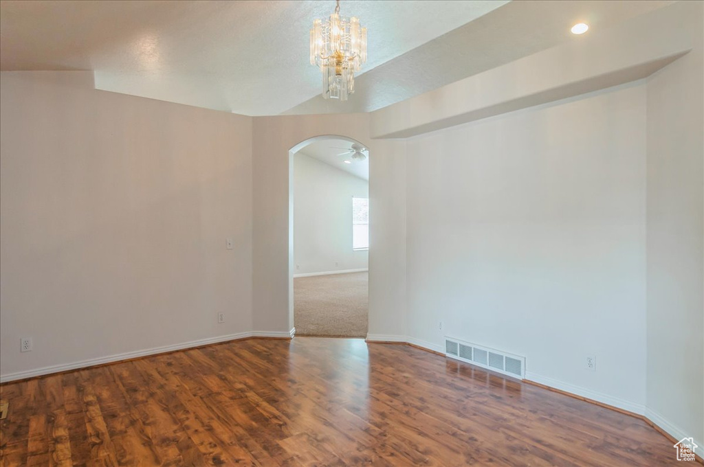 Unfurnished room featuring arched walkways, a chandelier, baseboards, wood finished floors, and vaulted ceiling