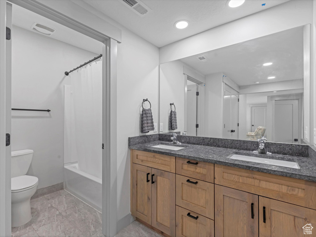 Bathroom featuring toilet, double vanity, baseboards, recessed lighting, and shower / tub combo