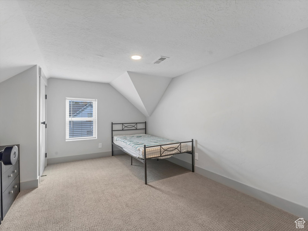 Carpeted bedroom with lofted ceiling, a textured ceiling, and baseboards