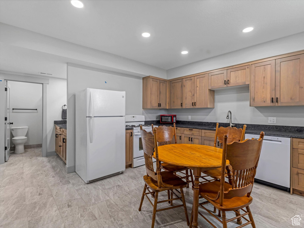 Kitchen featuring white appliances, dark countertops, recessed lighting, and brown cabinets
